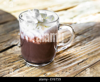 chocolate drink with whipped cream in transparent cup on rough wooden table Stock Photo