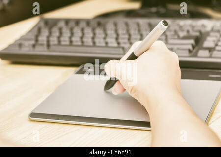 Retro image of female hand of a designer drawing with the stylus on a grey graphics tablet Stock Photo