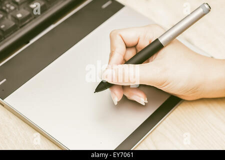 Retro image of female hand of a designer drawing with the stylus on a grey graphics tablet Stock Photo