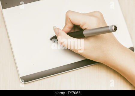 Retro image of female hand of a designer drawing with the stylus on a grey graphics tablet Stock Photo