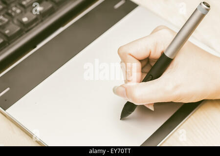 Retro image of female hand of a designer drawing with the stylus on a grey graphics tablet Stock Photo