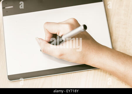 Retro image of female hand of a designer drawing with the stylus on a grey graphics tablet Stock Photo