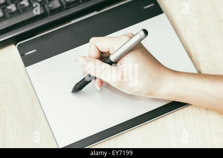 Retro image of female hand of a designer drawing with the stylus on a grey graphics tablet Stock Photo