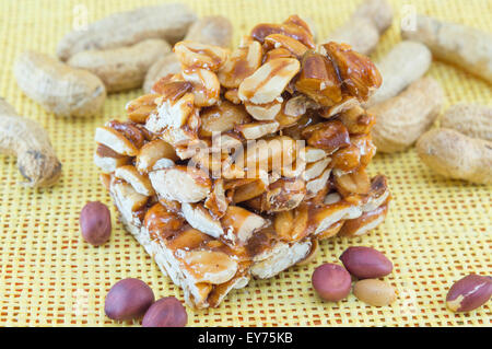 Honey bar with peanuts almonds and hazelnuts surrounded by bunch of roasted and raw peanuts on yellow background Stock Photo