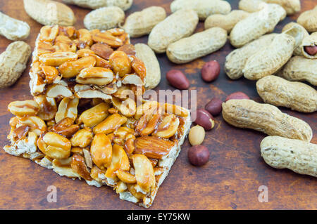 Honey bar with peanuts almonds and hazelnuts surrounded by bunch of roasted and raw peanuts placed on a wooden board Stock Photo