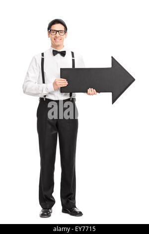 Full length portrait of a elegant young man with black bow-tie and suspenders holding a big black arrow pointing right Stock Photo