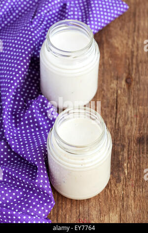 Homemade yogurt with chopped prunes in two small glass jars on a wooden table with purple cloth, selective focus Stock Photo