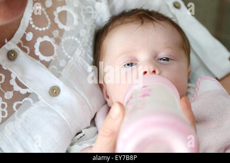 A very young baby being fed milk from a bottle. The parent is holding it an an angle with the baby on its back lying in her arms and feeding Stock Photo