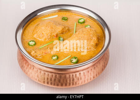 Overhead view of Indian chicken curry served in authentic copper bowl. Chopped green chilli used as garnish. Stock Photo