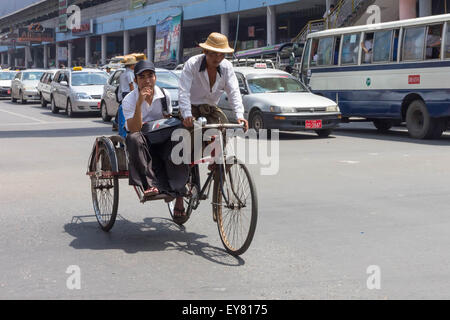 Yangon, Myanmar-May 7th 2014: A rickshaw carries a passenger to his destination. Rickdhaws are dying out in the city. Stock Photo