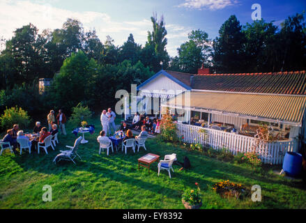 Friends sharing food, coffee and conversation at summer house on Tranholmen island in Stockholm Archipealgo in Baltic Sea waters Stock Photo