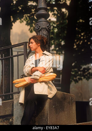 Parisian woman with baguettes resting against street lamp post in quiet Montmartre square Stock Photo