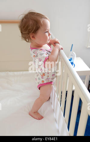 Side view shot of baby girl standing inside her cot looking inquisitive Stock Photo