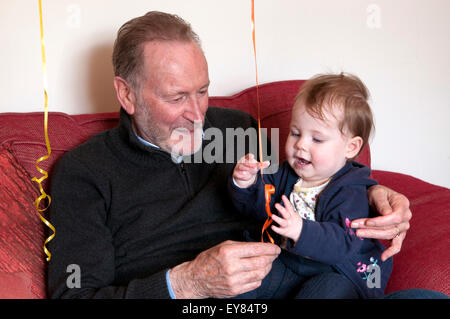 Baby girl sitting on her grandfathers lap playing with a balloon Stock Photo