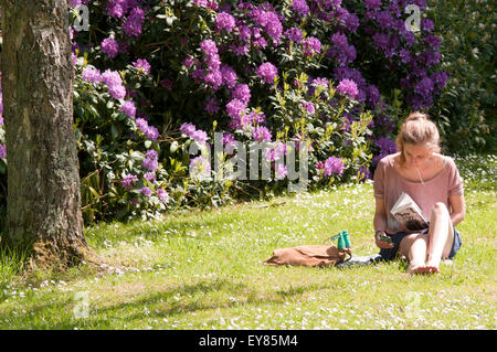 Young woman, university student, sitting on the grass reading Stock Photo