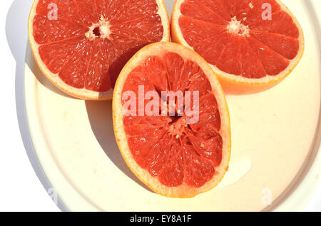 Halves of  red grapefruit with squeezed one and its juice, set on plate Stock Photo