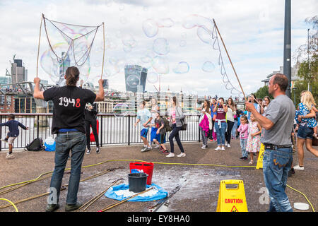 Street entertainers blowing huge bubbles entertaining children and for tips, Bankside, South Bank, London, UK in summer Stock Photo