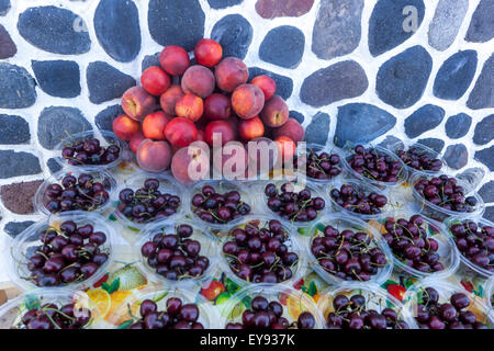 Fresh cherries in plastic bowls and a pyramid of nectarines for sale in Fira. Local fruit market. Santorini Island, Greece Stock Photo