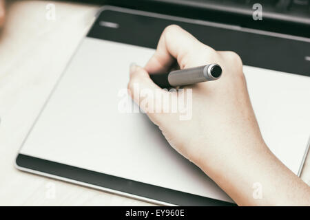 Retro image of female hand of a designer drawing with the stylus on a grey graphics tablet Stock Photo