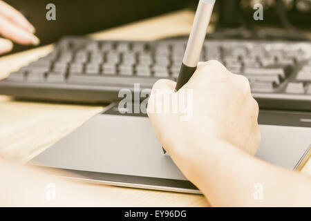 Retro image of female hand of a designer drawing with the stylus on a grey graphics tablet Stock Photo