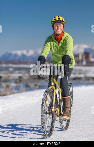 A Young Woman rides a studded tire bicycle down the Tony Knowles Coastal Trail, Anchorage, Southcentral Alaska, USA. Stock Photo