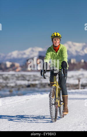 A Young Woman rides a studded tire bicycle down the Tony Knowles Coastal Trail, Anchorage, Southcentral Alaska, USA. Stock Photo