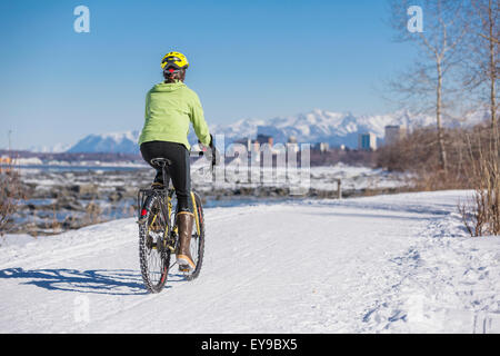 A Young Woman rides a studded tire bicycle down the Tony Knowles Coastal Trail, Anchorage, Southcentral Alaska, USA. Stock Photo