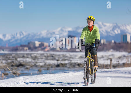 A Young Woman rides a studded tire bicycle down the Tony Knowles Coastal Trail, Anchorage, Southcentral Alaska, USA. Stock Photo