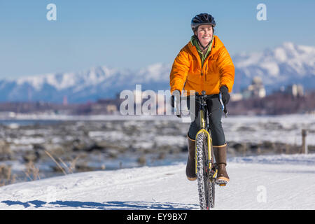 A Young Woman rides a studded tire bicycle down the Tony Knowles Coastal Trail, Anchorage, Southcentral Alaska, USA. Stock Photo