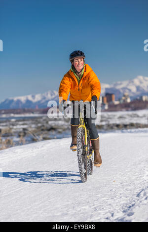 A Young Woman rides a studded tire bicycle down the Tony Knowles Coastal Trail, Anchorage, Southcentral Alaska, USA. Stock Photo