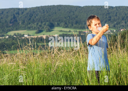 Boy using inhaler for asthma in village with summer sunset Stock Photo