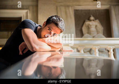 Portrait of Shy Attractive Young Man Leaning on Folded Arms Against Polished Marble Staircase Railing Inside Classical Building Stock Photo