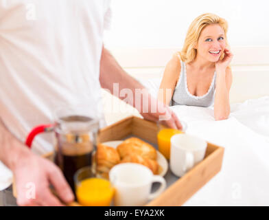 View of a Man bringing young attractive woman breakfast in bed Stock Photo