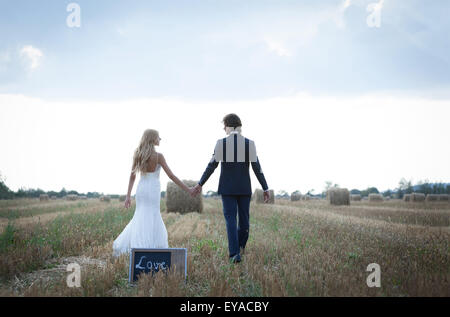 Married couple taking a walk on a field of hay bales, leaving back a mini blackboard that is written the word “love”. Stock Photo