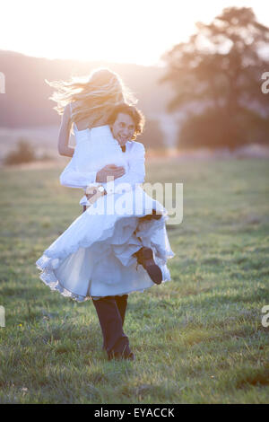 Married couple acting free and happy. The groom carries his bride on his shoulder. Stock Photo