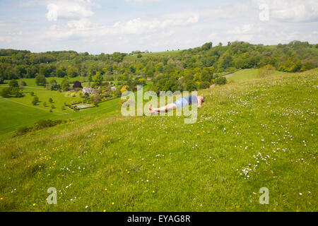 Woman lying on chalk grassland looking into deep green valley containing Rainscombe House, Oare Hill, Wiltshire, England, UK Stock Photo