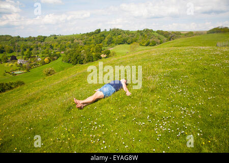 Woman lying on chalk grassland looking into deep green valley containing Rainscombe House, Oare Hill, Wiltshire, England, UK Stock Photo