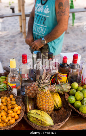 BAHIA, BRAZIL - MARCH 17, 2015: Brazilian beach vendor stands behind stall making cocktails featuring local tropical fruits. Stock Photo