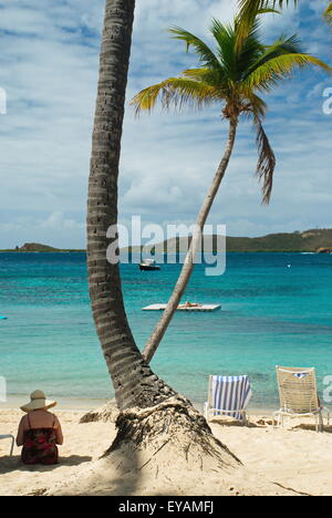 Woman wearing hat sitting in shade of palm tree on the beach of the Caribbean on the island of St. Thomas, US Virgin Islands. Stock Photo