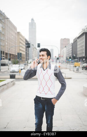 Knee figure of a young handsome indian contemporary business man walking through the city talking smarpthone looking on his right -  technology, network, business, finance concepts Stock Photo