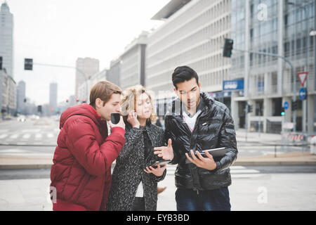 Multiracial contemporary business people working outdoor in town connected with technological devices live tablet and smartphone, looking on the screen - business, finance, technology concept Stock Photo