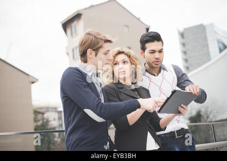 Multiracial contemporary business people working outdoor in town connected with technological devices like tablet, talking to each other - business, finance, technology concept Stock Photo