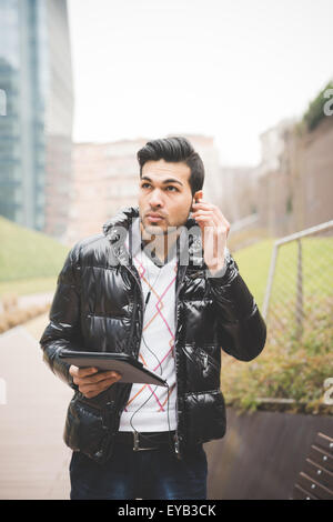 Half Lenght  of a young handsome indian businessman listening music with earphones while working on a tablet connected online overlooking - business, work, study, technology concept Stock Photo