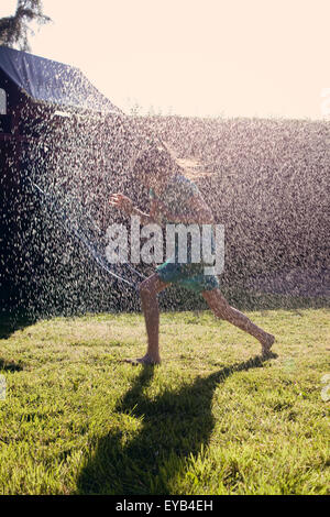 Girl running through water spray from a garden sprinkler. Stock Photo