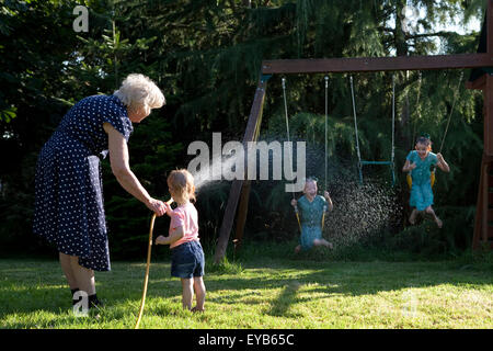 Family playing in garden with water hose in summer. Stock Photo