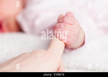 A very young baby gripping her mothers finger showing her tiny nails on her clenched hand. The blurred baby is asleep in the background