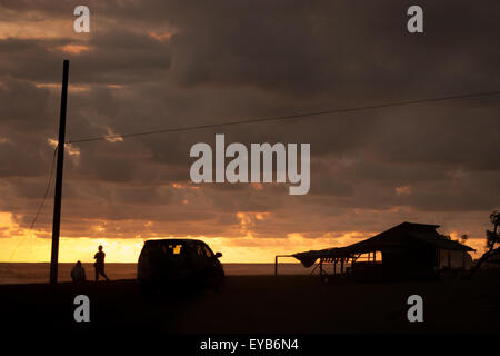 Gloomy sunset with people, car, and wooden shelter on beach. Indian Ocean view in Bengkulu, Sumatra. Stock Photo