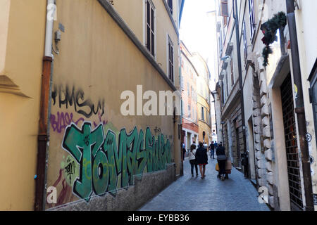 Pedestrians walking down a narrow street with graffiti on one wall. Stock Photo