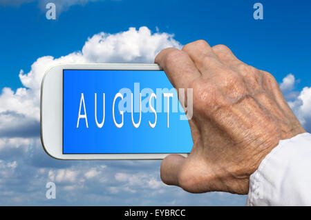 Smart phone in old hand with month of the year - August on screen. Selective focus. Stock Photo