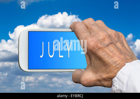 Smart phone in old hand with month of the year - July on screen. Selective focus. Stock Photo